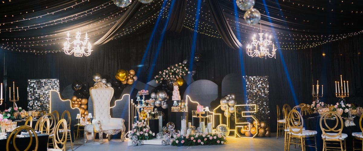 Black-draped party venue features mirrored disco balls, blue spotlights, gold seating, flowers, and a glowing 15.